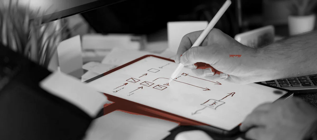 A developer sketching a flow by hand, application code open on the monitor behind