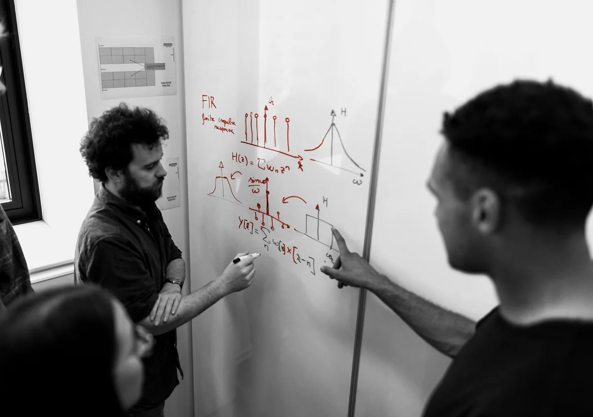 Engineers working a derivation through on a whiteboard, the reasoning written in marker